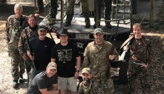 Group of men posing outdoors with hunting gear.