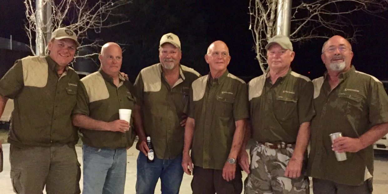 A group of six men in matching shirts posing outdoors at night.