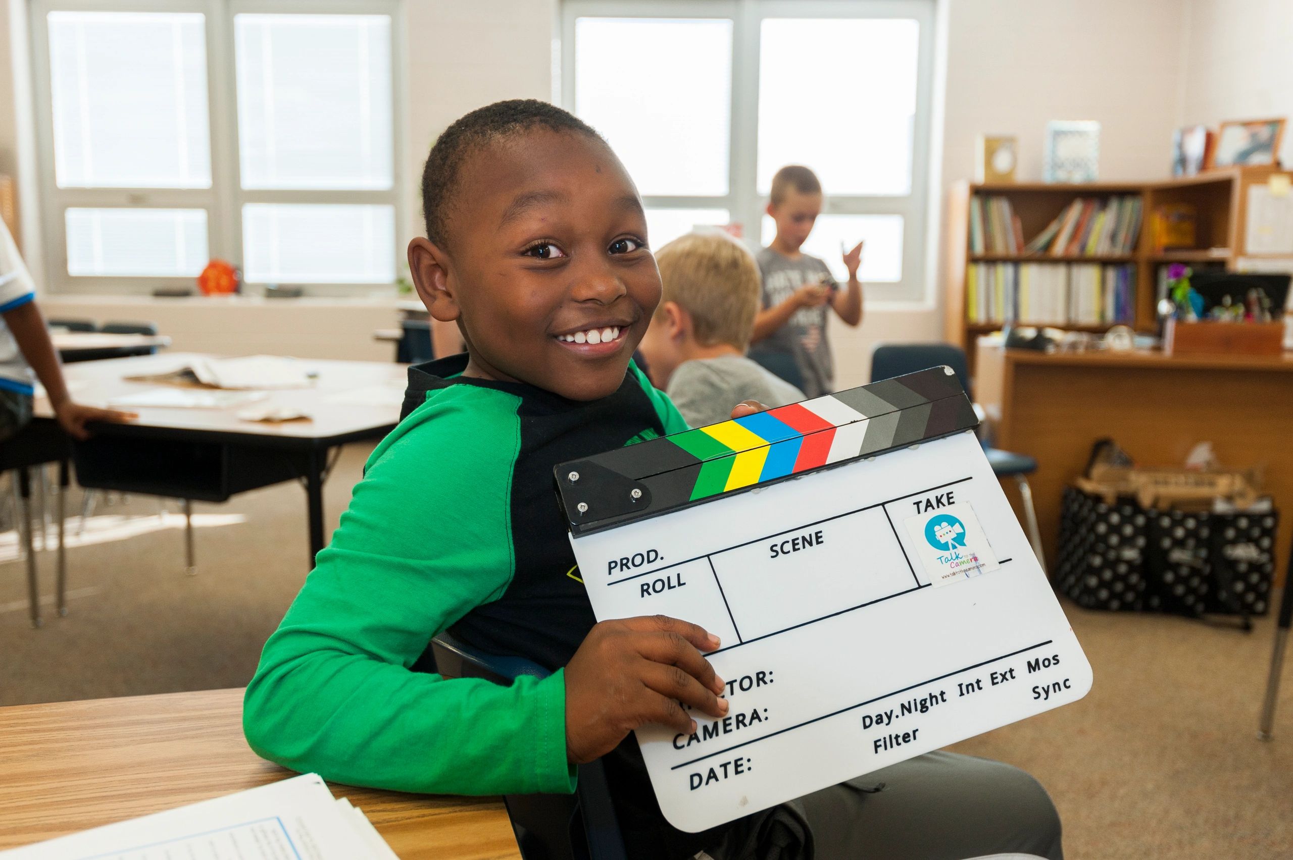A young student in one of our movie magic classes, smiling at the camera with a clapboard in hand.
