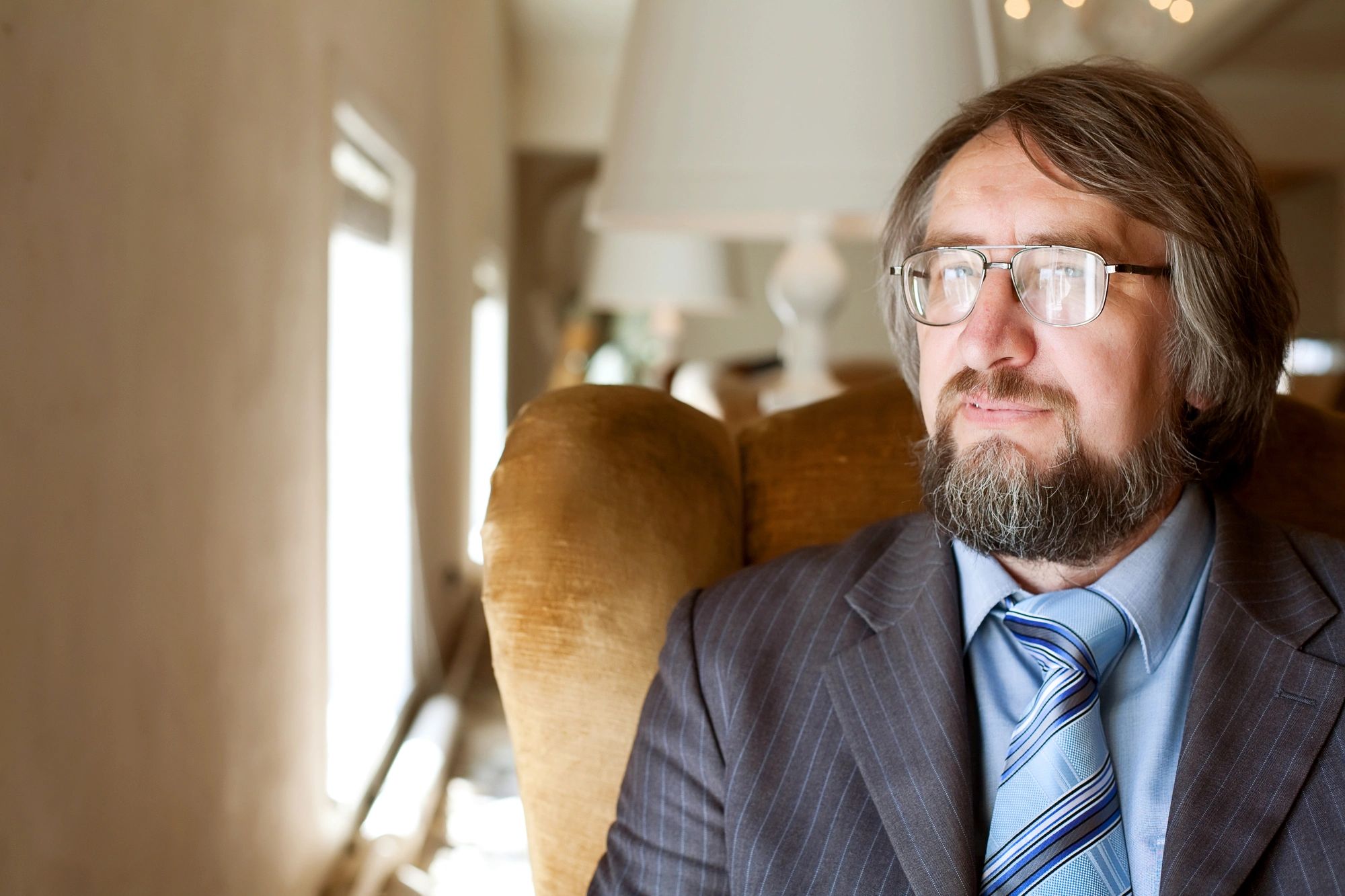 A man with blazer wearing glasses sitting on the sofa