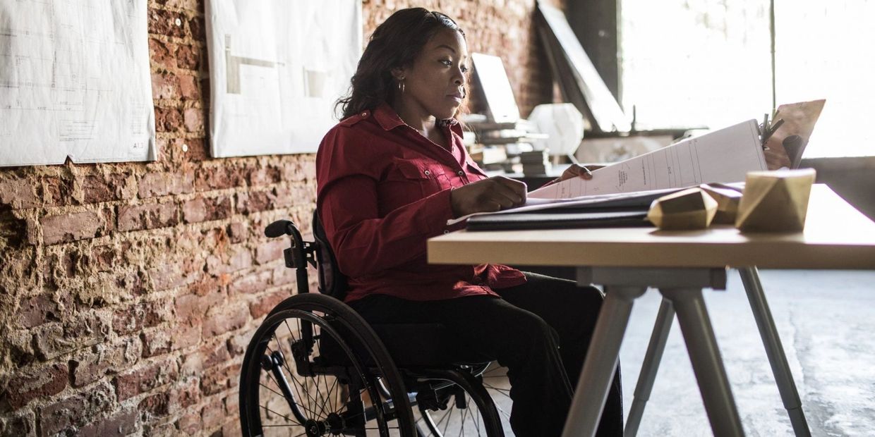 A Black Woman sitting in a wheelchair reading a blueprint