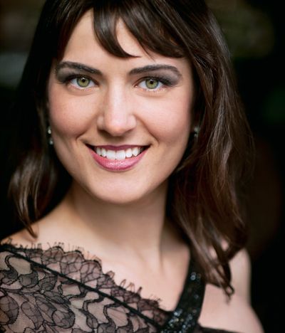 Woman with striking green eyes and lace dress smiling.