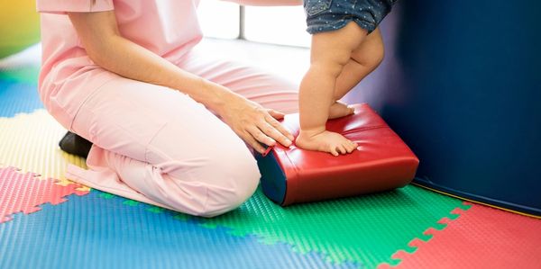 baby legs stepping on a red foam pillow assisted with an adult