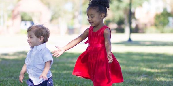 a baby boy wearing a white polo shirt and jeans and a little girl wearing a red dress walking