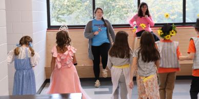 Children in costumes following two adults in a classroom setting.