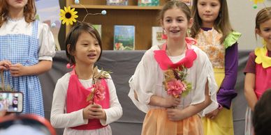 Children dressed in colorful costumes holding flowers in a school play.