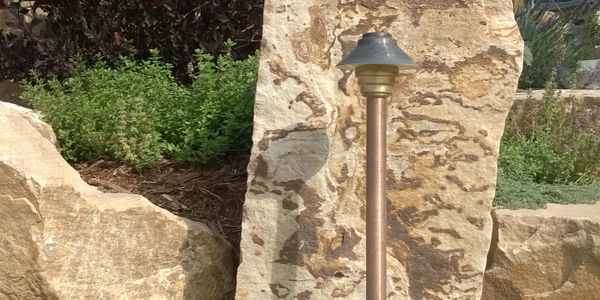 Vista path light in a garden with native plantings and buff flagstone slabs.