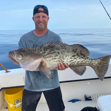 Fishing charter customer holding a large grouper that he caught.