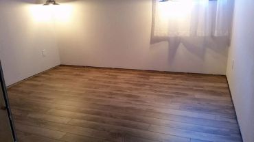 Chambre vide avec parquet en bois et lumière douce.