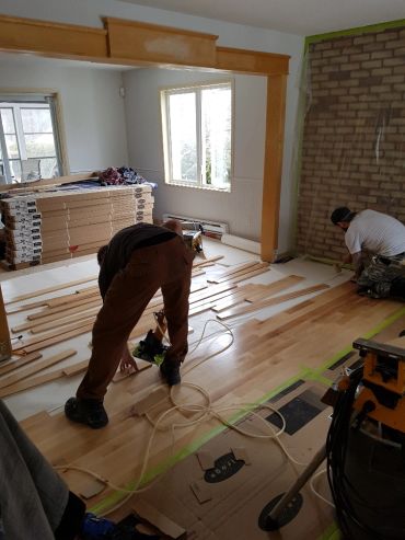 Deux ouvriers posent un parquet en bois dans une pièce en rénovation.