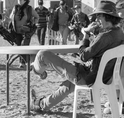 Man in a hat sitting on a plastic chair with legs stretched out.
