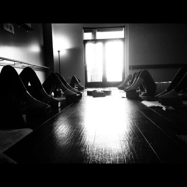 People lying down in a dimly lit room with light streaming through a door.