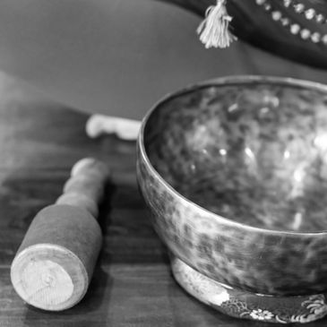 A metal singing bowl with a wooden mallet on a table.