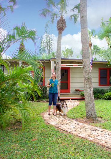 Ali holds a mug of coffee while walking a Sheltie in front yard of the Lily Patch Bungalow on Siestay