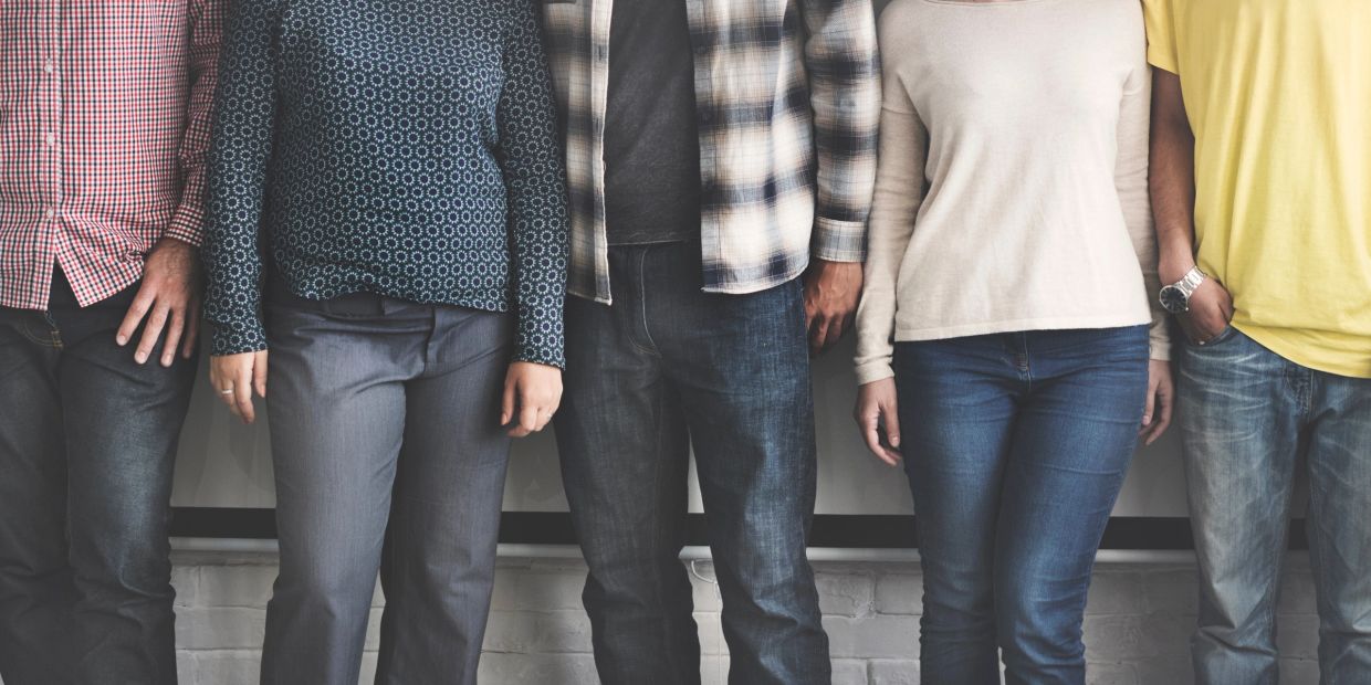 Five casually dressed people standing side by side against a wall.