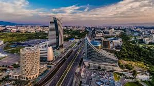 A modern cityscape with unique architectural buildings and a highway.
