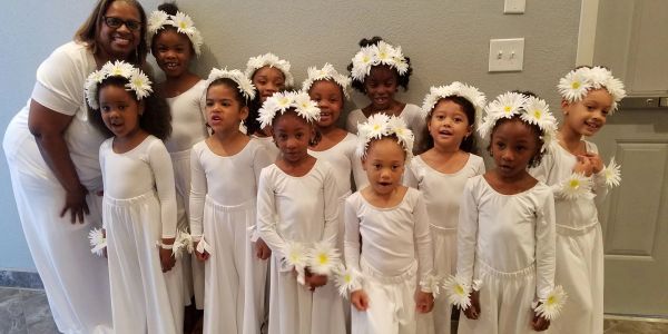 A group of young girls and a woman dressed in white with flower headbands.