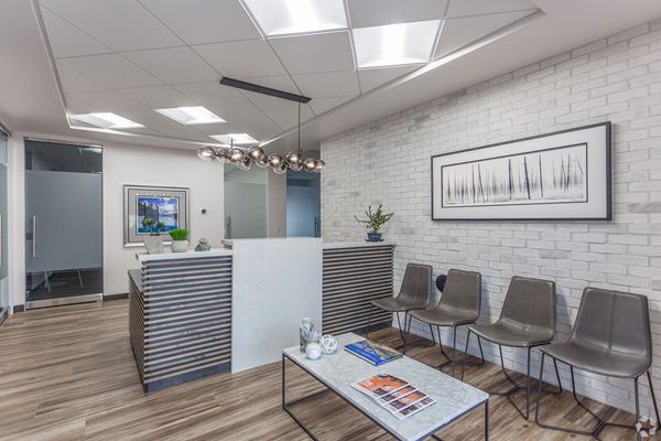 Upscale lobby area with 4 brown chairs, a granite adorned front desk below a modern light fixture