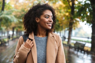 Woman smiling, looking to the side, well-dressed with a smile and clutching the handle of a backpack