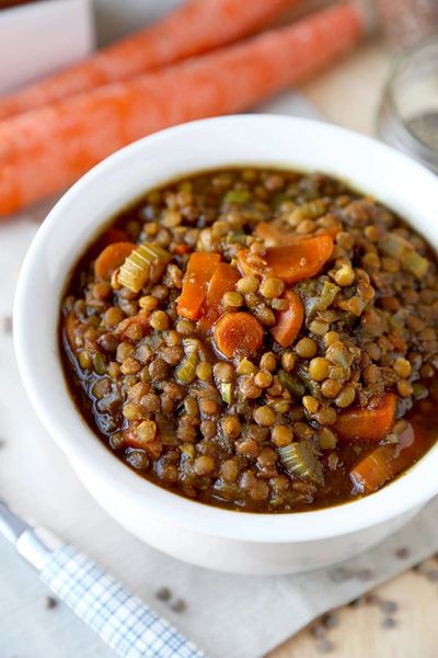 Cooked lentil soup in a white bowl with sliced cooked carrots on top.