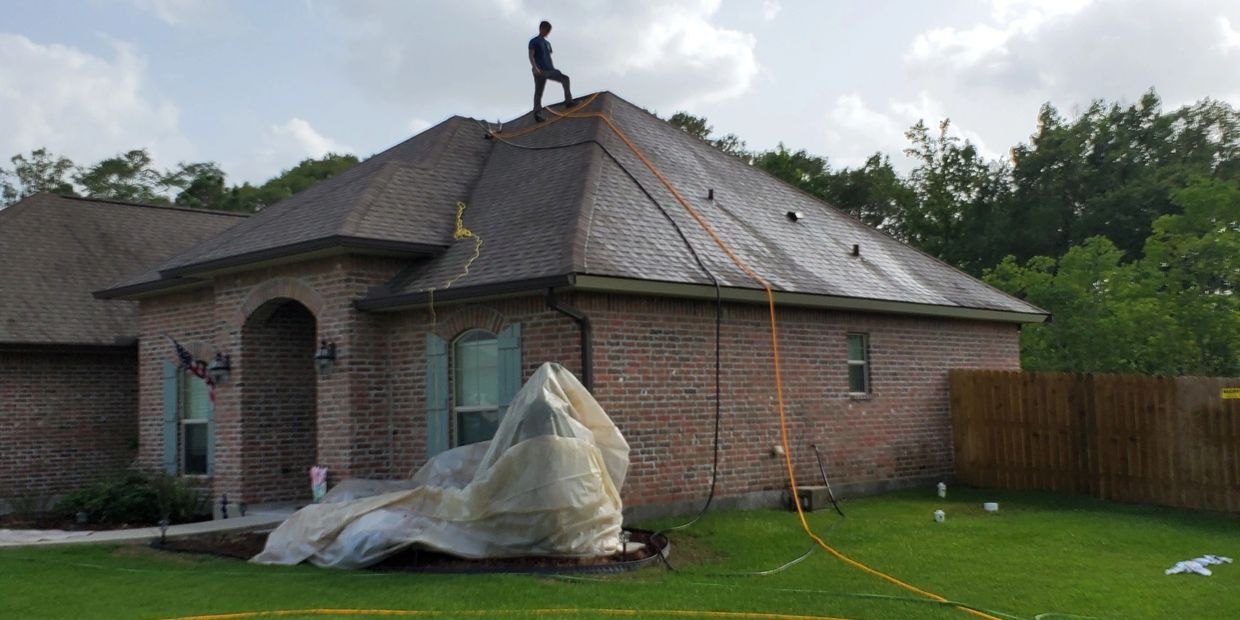 Employee applying cleaning solution to a shingle roof