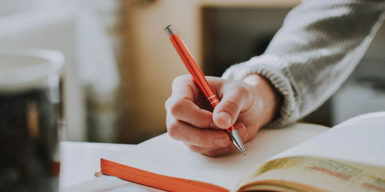 Picture of a hand holding a pen and writing in a notebook 