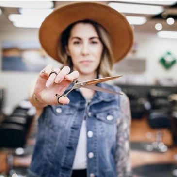 Woman in a hat holding scissors in a barbershop.