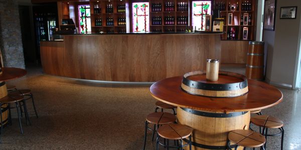 Cellar door tasting room with timber bar, wine display shelves, and barrel tables with stools.