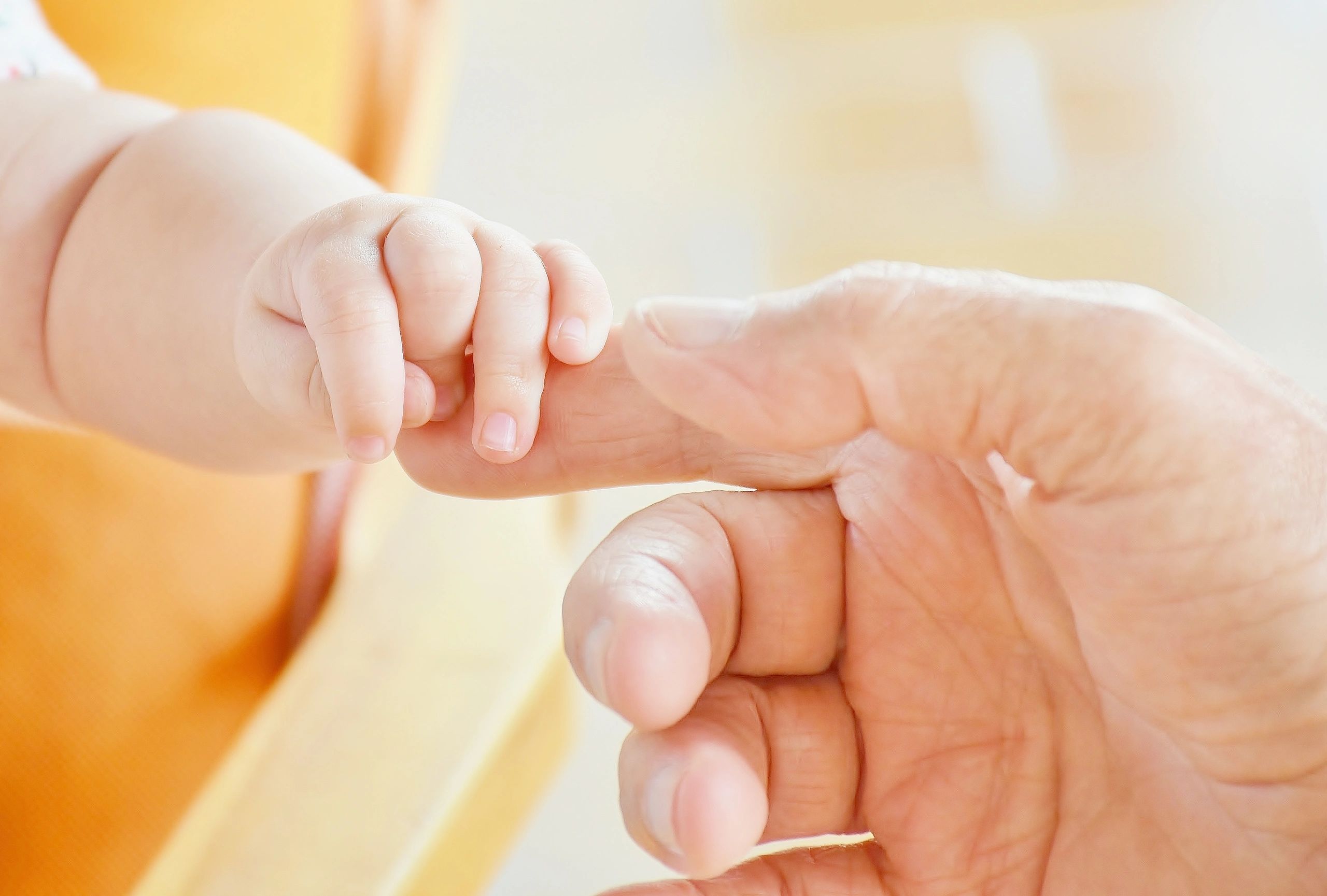 Infant hand gripping index finger on hand of an aged person