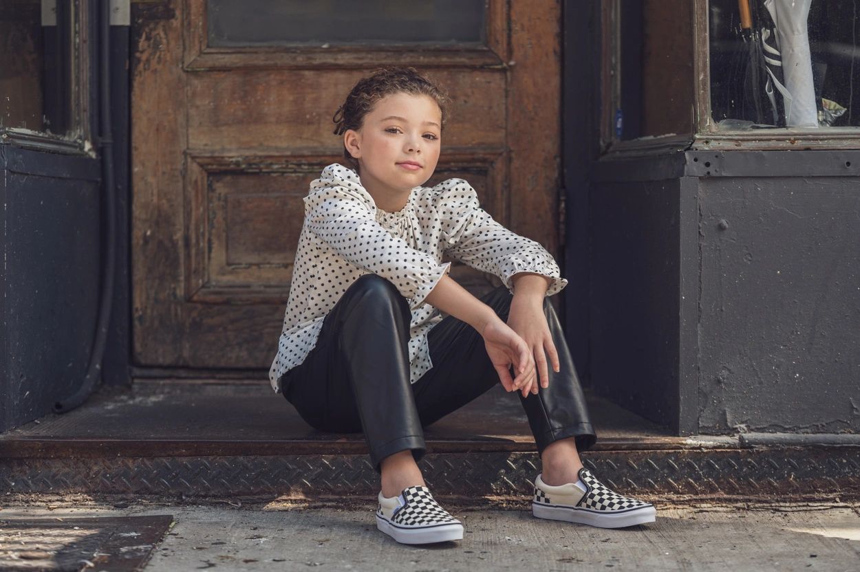 Kid female model, in black pants and polka dot shirt sitting on stoop in Lower East Side, NYC