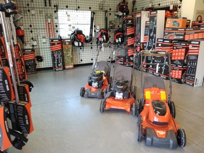 Image of inside of store showing weed eaters, trimmers, blowers hanging on wall, mowers on floor.