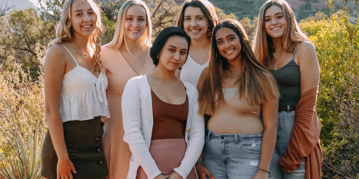 Group of six young women posing outdoors, smiling.