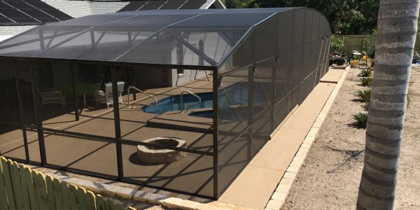 Swimming pool screen enclosure, with concrete pool deck and fire pit. Pool screen.