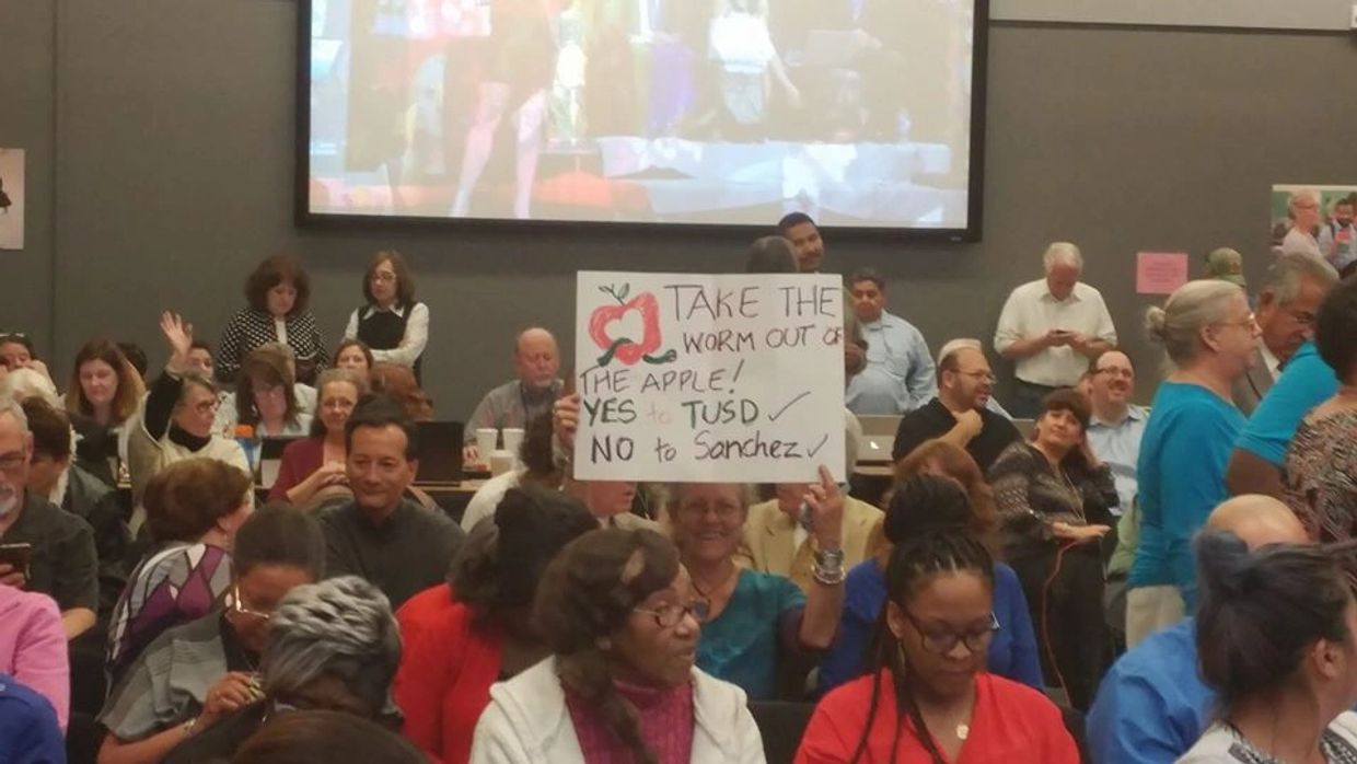 A woman holds a protest sign at a crowded meeting.