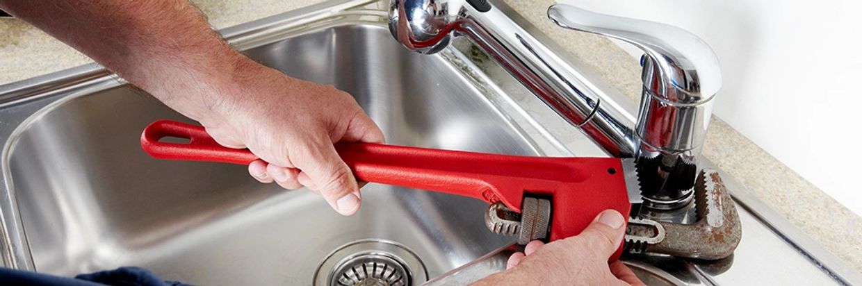 Red pipe wrench on kitchen tap faucet during residential plumbing repair by KaiTech Plumber