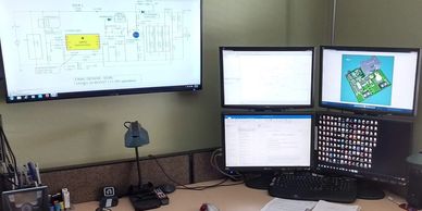 Schematic capture and PCB layout displayed on PC monitor screens.