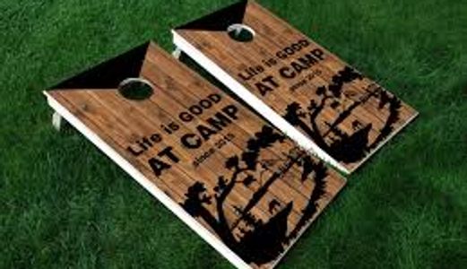 Two wooden cornhole boards with camping-themed design on grass.