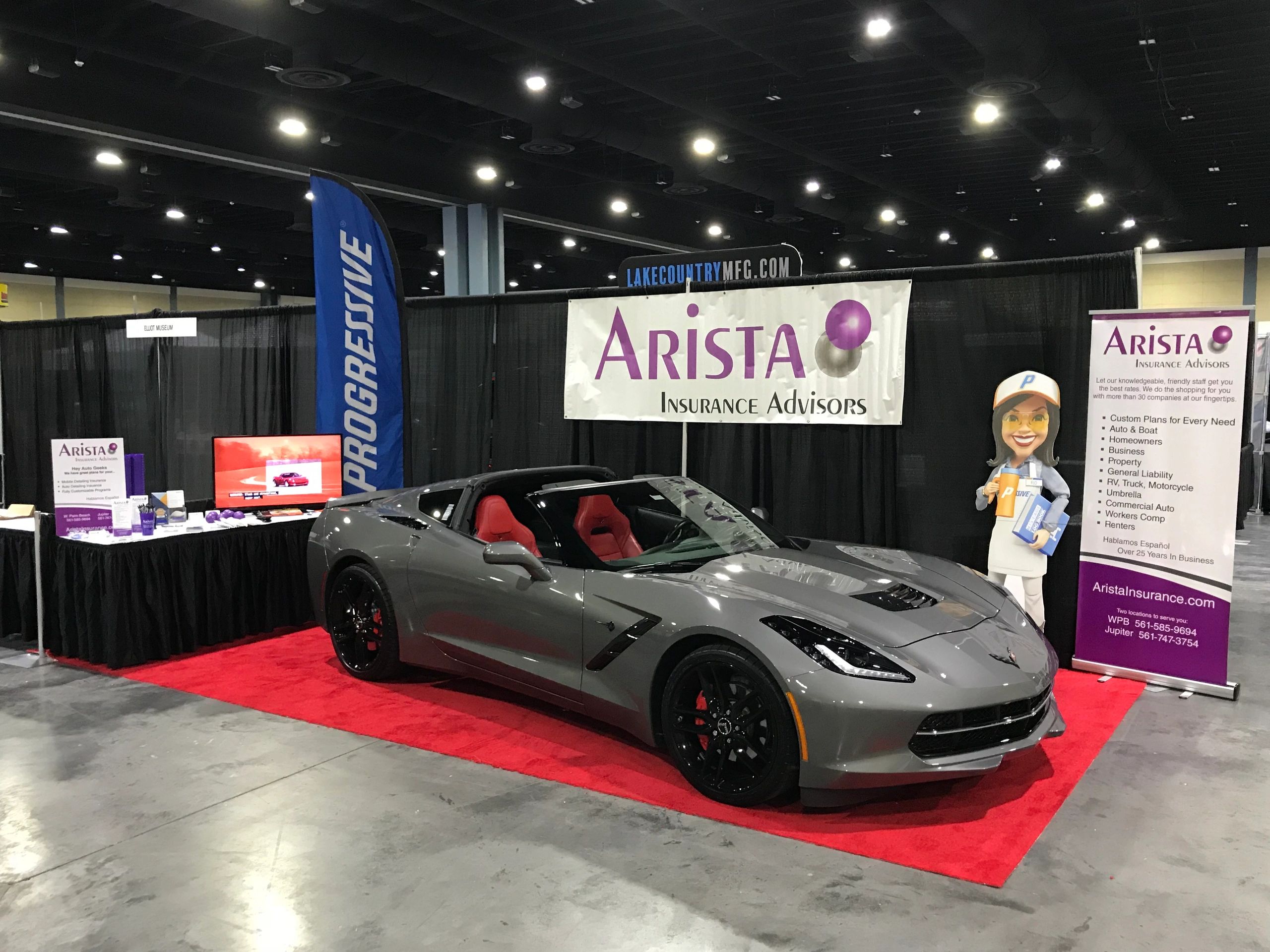 A gray Corvette Stingray in an Autoshow booth with an Arista Insurance Advisors banner