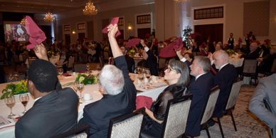 Guests raising napkins at a formal banquet event in an elegant hall.