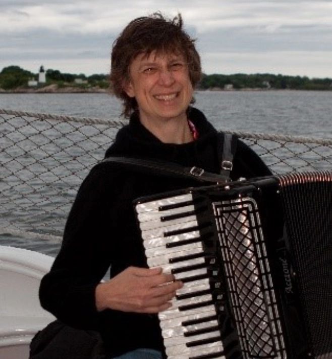 Person playing accordion on a boat with water and land in the background.
