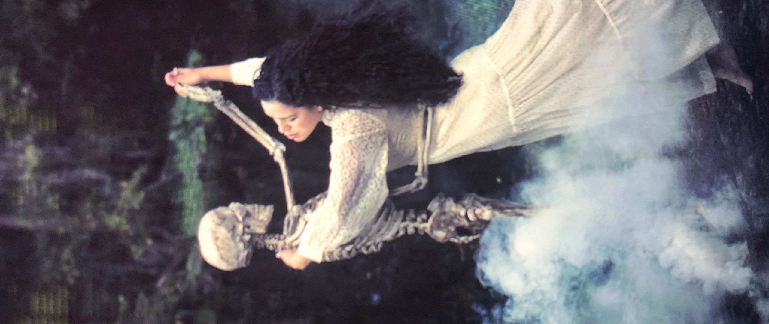Woman dancing with a skeleton in a misty forest.