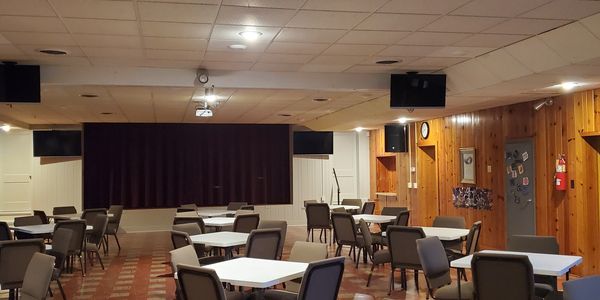 Empty event hall with tables and chairs arranged, and a stage with a microphone.