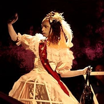 Person in vintage dress with a feathered headpiece performs on stage.