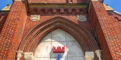 Gothic-style red brick church entrance with a crown emblem.