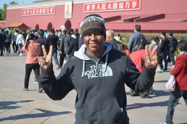 Man in a black hoodie making peace signs in a busy outdoor area.