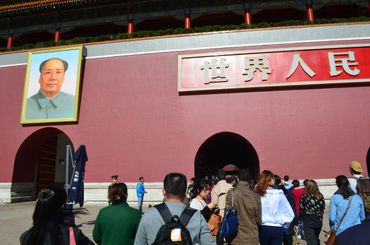 Crowd walking toward a large red wall with Mao Zedong's portrait in Tiananmen Square.