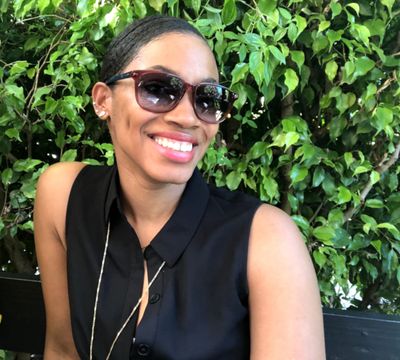 Smiling woman wearing sunglasses and a black sleeveless top.