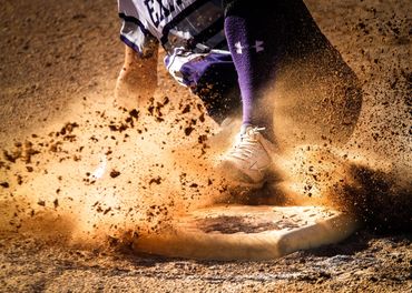 Base runner sliding into a base, playing baseball with dirt flying.