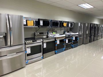 A row of modern kitchen appliances including refrigerators, ovens, and microwaves in a showroom.