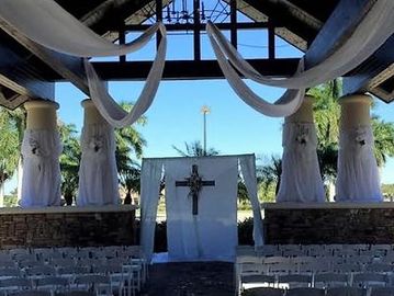 Outdoor wedding altar decorated with white fabric and cross under a pavilion.